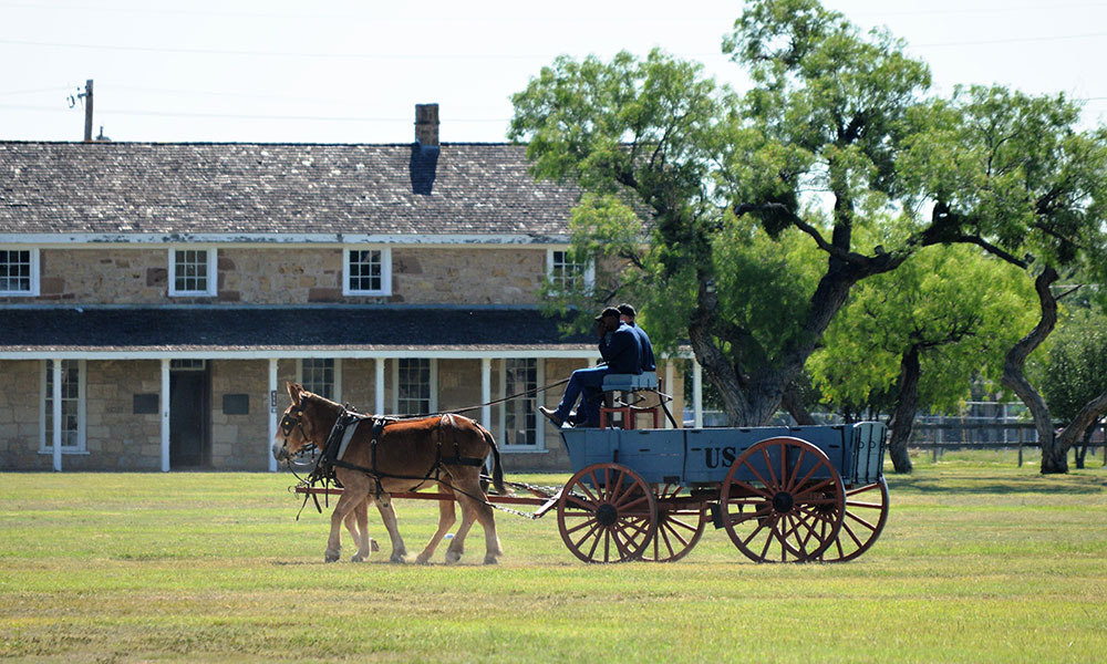 Stage coach with horses in front of building with trees